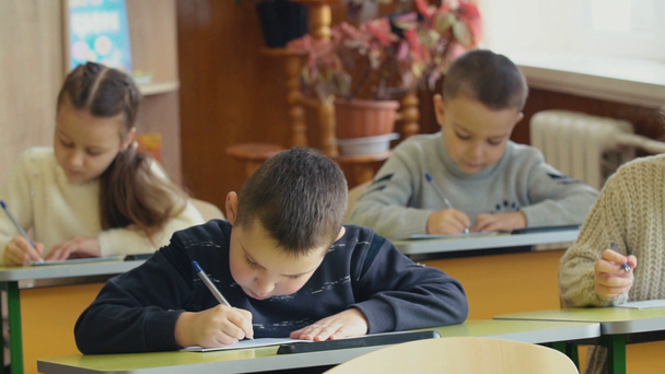 Dzieci pisać siedząc przy biurku - Materiał filmowy, wideo