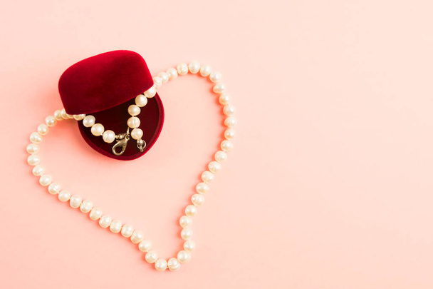 Heart of pearls necklace with opened gift box on pink background with copy space - Photo, image