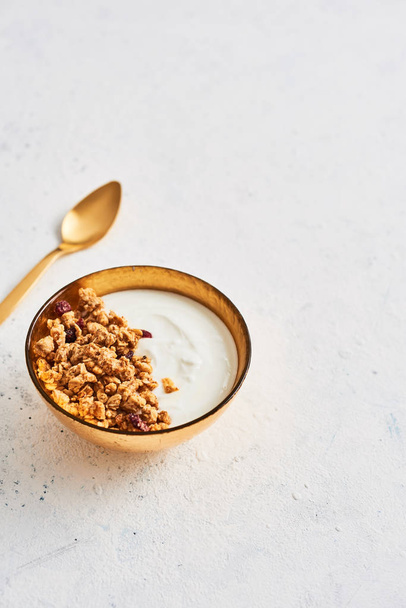 Healthy breakfast. Muesli with Greek yoghurt and honey in golden bowl with golden spoon on white abstract background. Top view. Copy space for text. - Zdjęcie, obraz