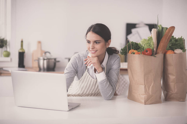 Smiling woman online shopping using computer and credit card in kitchen - Foto, Imagen