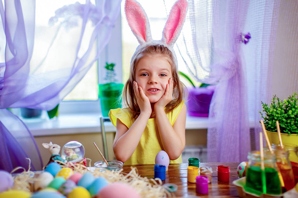 Happy easter girl in bunny ears painting eggs, small child at home. spring holiday - Фото, изображение