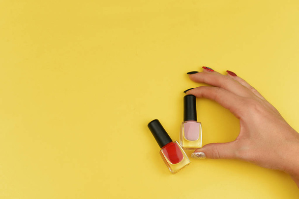 girl holding trendy bottles with gel varnish red for female nails on a yellow background - Foto, Imagem