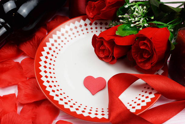 романтический ужин с красными розами и лепестками на столе с доком вина и сердцем на праздник Святого Валентина в феврале
 - Фото, изображение