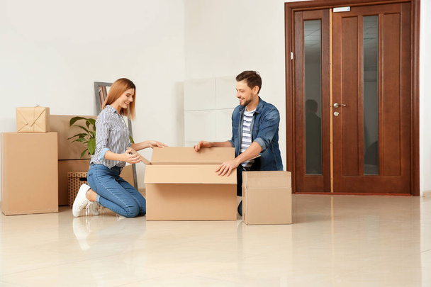 Happy couple unpacking moving box in their new house - Фото, изображение