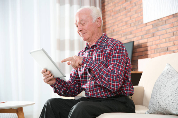 Elderly woman using smartphone on sofa in living room - Foto, afbeelding