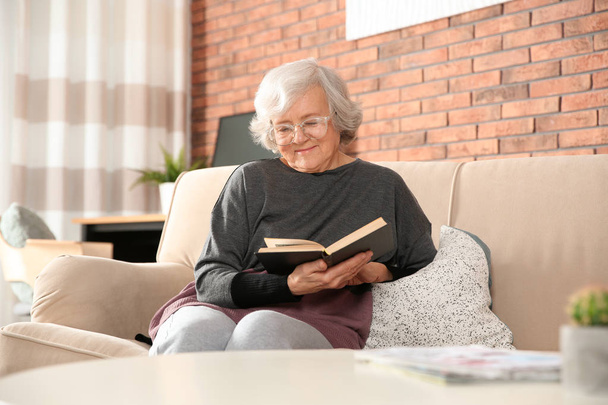 Elderly woman using smartphone on sofa in living room - Valokuva, kuva