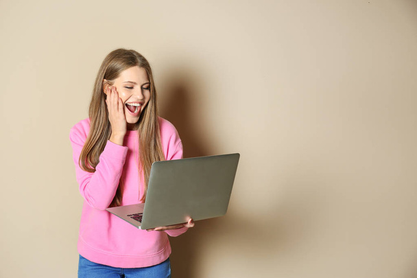 Emotional young woman with laptop celebrating victory on color background. Space for text - Photo, Image
