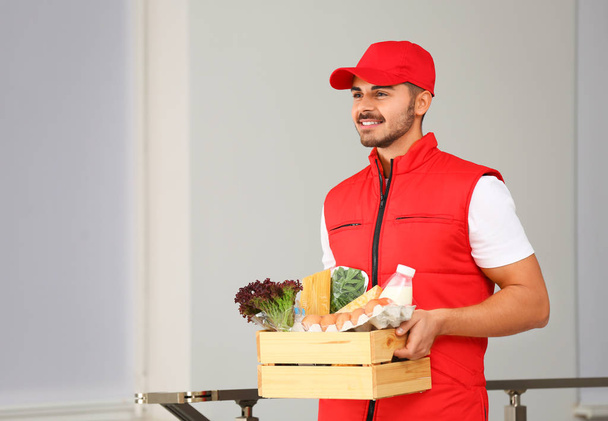 Food delivery courier holding wooden crate with products indoors. Space for text - Foto, Imagem