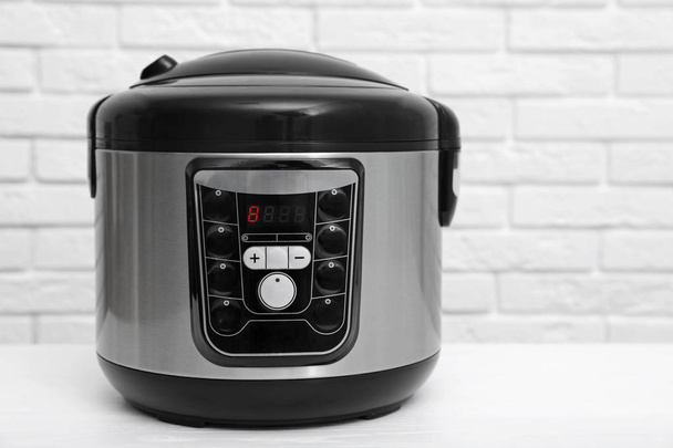 Modern electric multi cooker on table near brick wall - Photo, image