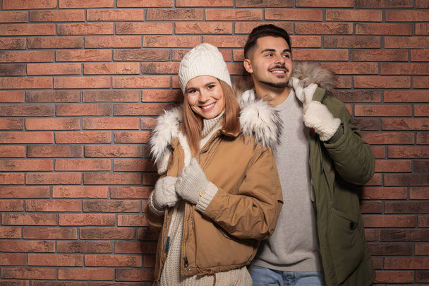 Young couple wearing warm clothes against brick wall, space for text. Ready for winter vacation - Foto, immagini