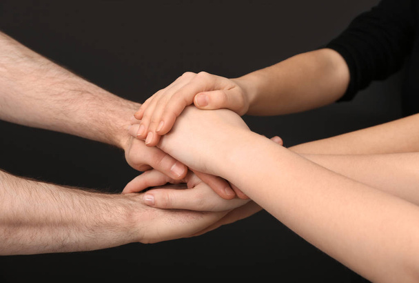 Young people putting their hands together on dark background, closeup - Φωτογραφία, εικόνα