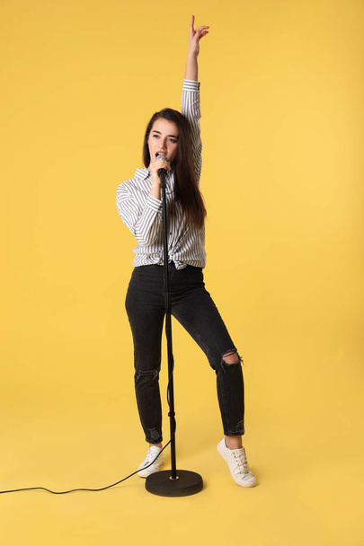 Young woman wearing casual clothes singing in microphone on color background - Foto, Imagem