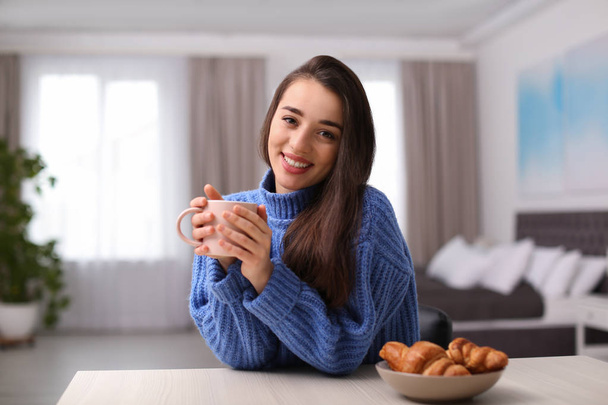 Young woman drinking coffee at table indoors. Winter season - Fotoğraf, Görsel