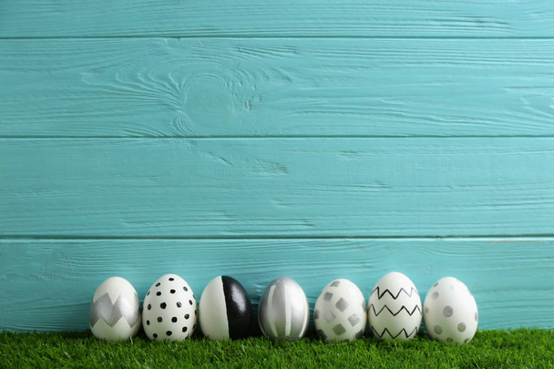 Line of painted Easter eggs on green lawn against wooden background, space for text - Fotoğraf, Görsel