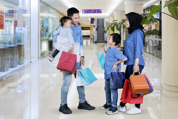 Picture of Muslim family holding shopping bags while talking each other in the mall - Фото, изображение