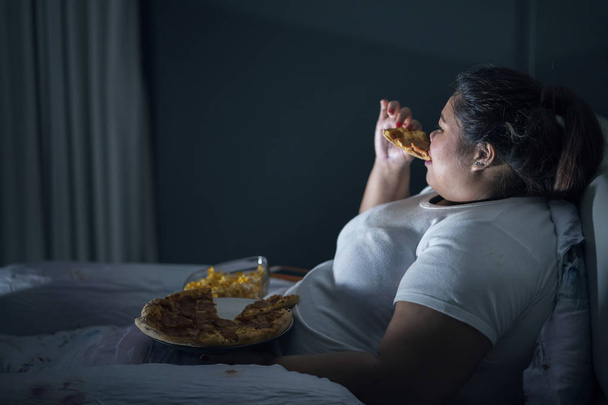 Unhealthy lifestyle concept: Obese woman eating pizza while watching TV in bed before sleep - Fotografie, Obrázek