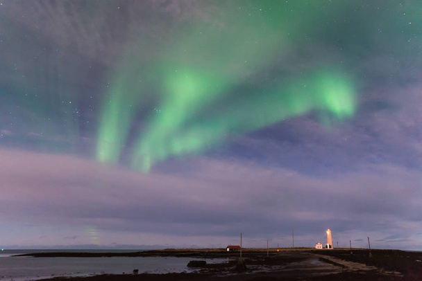 海のアイスランドのグロッタ灯台と手前の黒い砂のビーチに緑オーロラ - 写真・画像