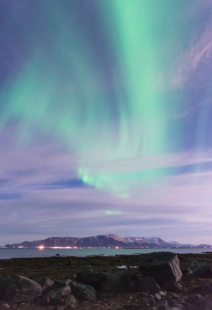Wirbel grüner Polarlichter über einem schwarzen Sandstrand, dem Meer und den Bergen außerhalb von Reykjavik, Island - Foto, Bild
