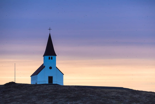 Lever de soleil violet et orange sur l'église Vik en Islande au sommet d'une colline, entouré de centaines d'oiseaux
 - Photo, image