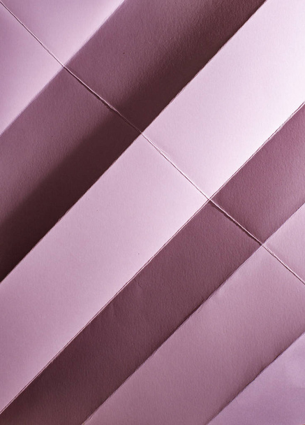 Folded pink colour paper. Pastel tones. Hard natural light. Folds and wrinkles on paper. Geometric shapes and figures on the paper. - Фото, изображение