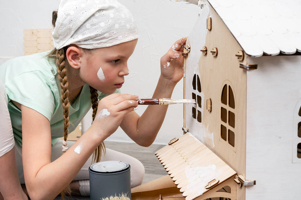 Children at work: The girl neatly paints the facade of the doll house with a small tassel in white. - Фото, изображение