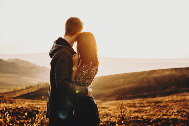 Αξιολάτρευτο νεαρό Καυκάσιος ζευγάρι αγκαλιάζει και κοιτάζοντας μακριά το έπος δείτε ονειρεύεται το ηλιοβασίλεμα στο χρόνο τις διακοπές τους. - Φωτογραφία, εικόνα