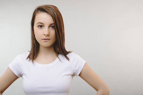 Close up of a cute girl dressed in white shirt posing seriously with hands on her shoulders against a white background. - 写真・画像