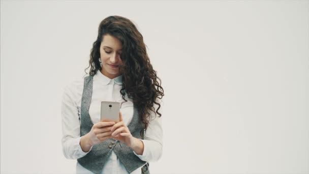 A young energetic girl with curly hair is photographed on the phone. Having made a sephi . On a white background. - Materiał filmowy, wideo