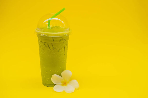 Green tea latte with ice in plastic cup and straw on yellow background. Homemade Iced Matcha Latte Tea with Milk take away - Foto, Bild
