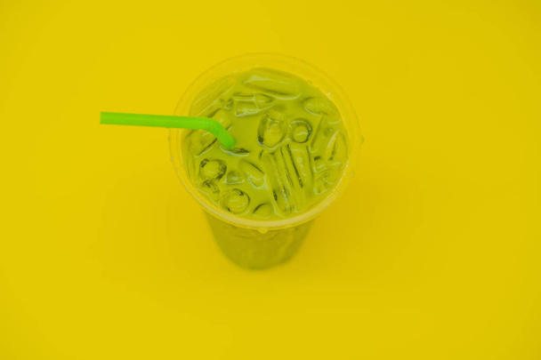 Green tea latte with ice in plastic cup and straw on yellow background. Homemade Iced Matcha Latte Tea with Milk take away - 写真・画像
