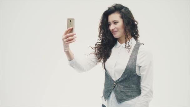 A young energetic girl with curly hair is photographed on the phone. Having made a sephi . On a white background. - Filmagem, Vídeo