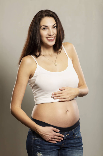 pregnancy and expectation concept - happy pregnant woman and touching her belly, gray background, vertical portrait - Фото, изображение