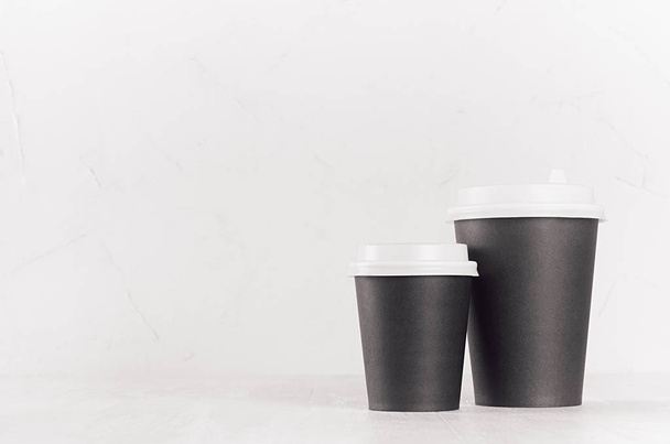 Coffee mockup - big and small blank black paper cups with white cap on white wood table with copy space, coffee shop interior. Modern elegant concept for branding identity, advertising, design. - Foto, Imagem