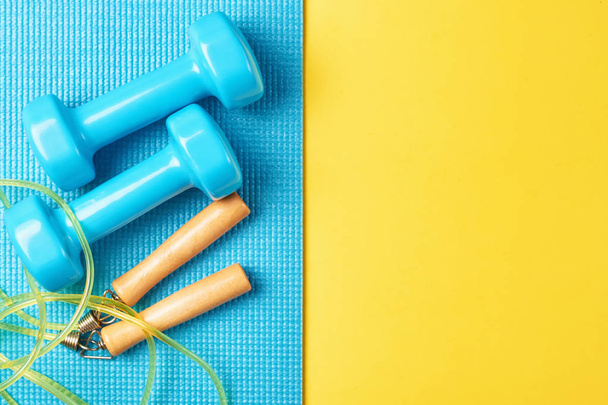 Flat lay, top view minimal background, fitness concept. Blue dumbbells and jump rope on blue and yellow background - Foto, imagen