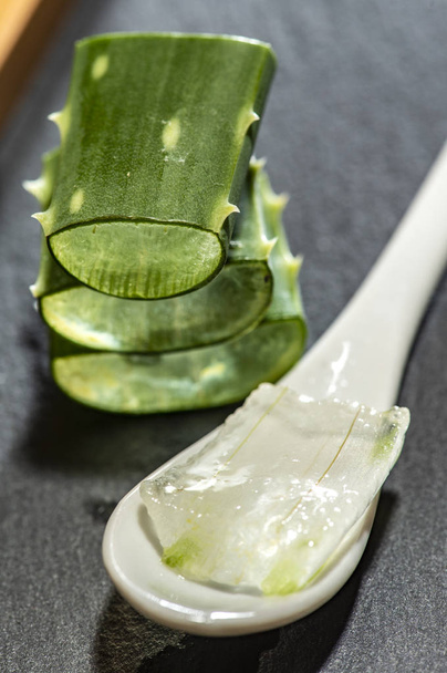 Aloe vera slices on dark background and spoon with aloe gel. Health and beauty concept. Closeup aloe pieces on backlight. - Foto, imagen