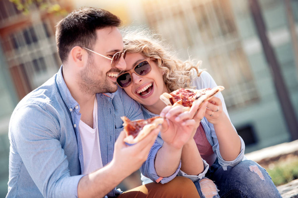 Beautiful loving couple sitting in the park and eating pizza.Dating,  food,lifestyle concept. - Photo, Image