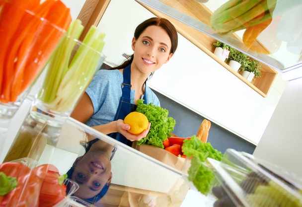 Portrait of female standing near open fridge full of healthy food, vegetables and fruits. Portrait of female - Foto, Bild