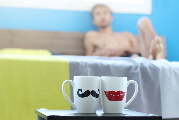 osamělý muž leží v posteli a vypadá na dva šálky ranní čaj nebo kávu na stole, sny o jeho chybějící přítelkyně, víkendové ráno v hotelu apartmány  - Fotografie, Obrázek