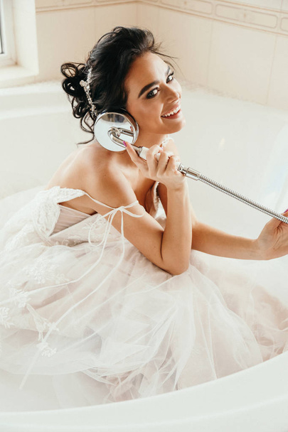 fashion interior photo of beautiful woman bride with dark hair in luxurious wedding dress posing in bath in bathroom - Foto, Imagem