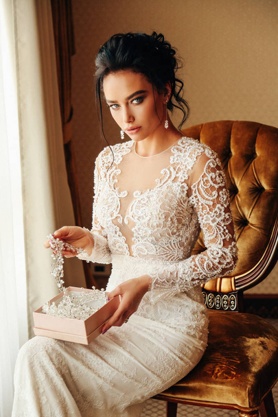 fashion photo of beautiful woman bride with long dark hair in luxurious wedding dress and accessories posing in elegant interior - Foto, imagen