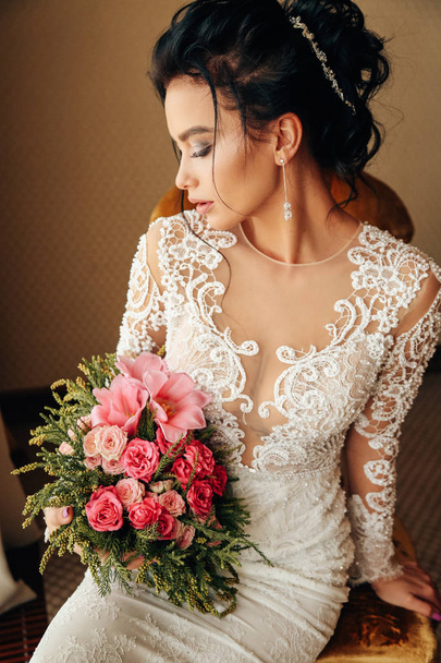 fashion photo of beautiful woman bride with long dark hair in luxurious wedding dress and accessories posing in elegant interior - Fotó, kép