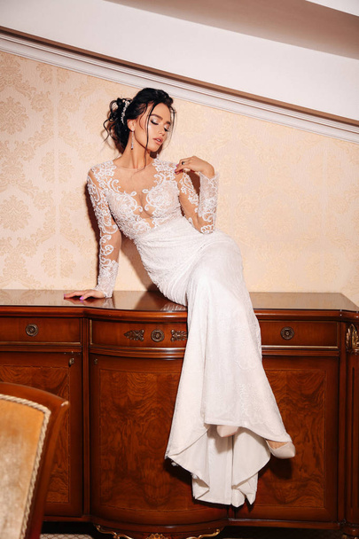 fashion photo of beautiful woman bride with long dark hair in luxurious wedding dress and accessories posing in elegant interior - Фото, зображення