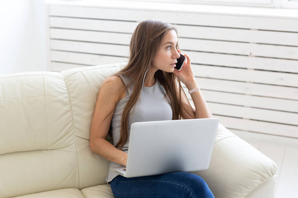 Business, freelance and people concept - Young woman sitting on sofa and talking on telephone - Photo, Image