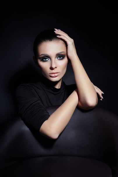 Classic Smokey makeup on woman face, beautiful big eyes. Fashion Perfect makeup, expressive eyes on girl face, smooth black eyebrows, licked brunette hair. Portrait of a woman on a dark background - Foto, imagen
