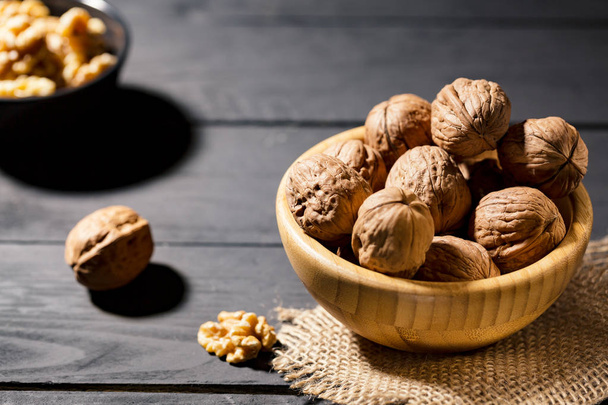 Whole organic nuts with shell  in a wooden bowls on black table selective focus. Copy space for text. - Foto, Imagem