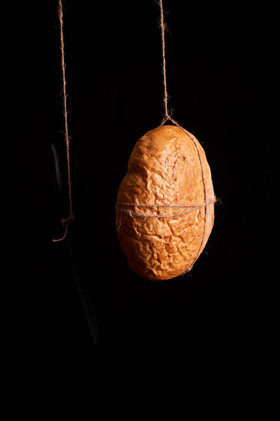 Round fresh bread with a kitchen table and a knife on a black background - Fotografie, Obrázek
