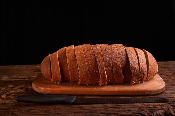 Pan rebanado sobre una mesa de madera y sobre un fondo negro
 - Foto, Imagen