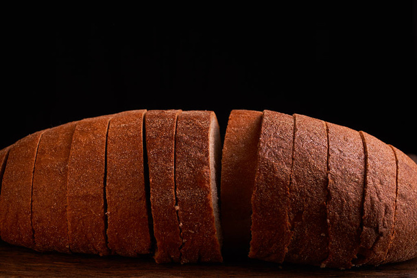 Нарізаний хліб на дерев'яному столі і на чорному тлі
 - Фото, зображення