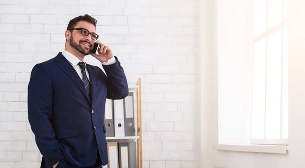 Предприниматель разговаривает с клиентом по телефону, стоит у окна
 - Фото, изображение