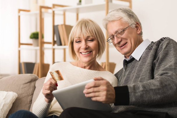 Modernes Senioren-Paar kauft online mit Tablet und Kreditkarte zu Hause ein - Foto, Bild